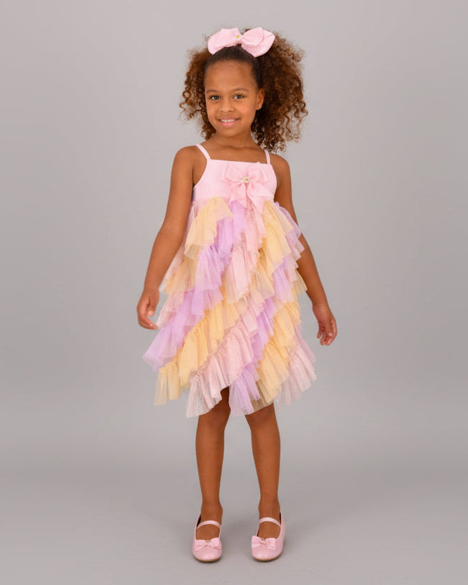 Young girl wearing a colorful dress with ruffles against a beige wall.