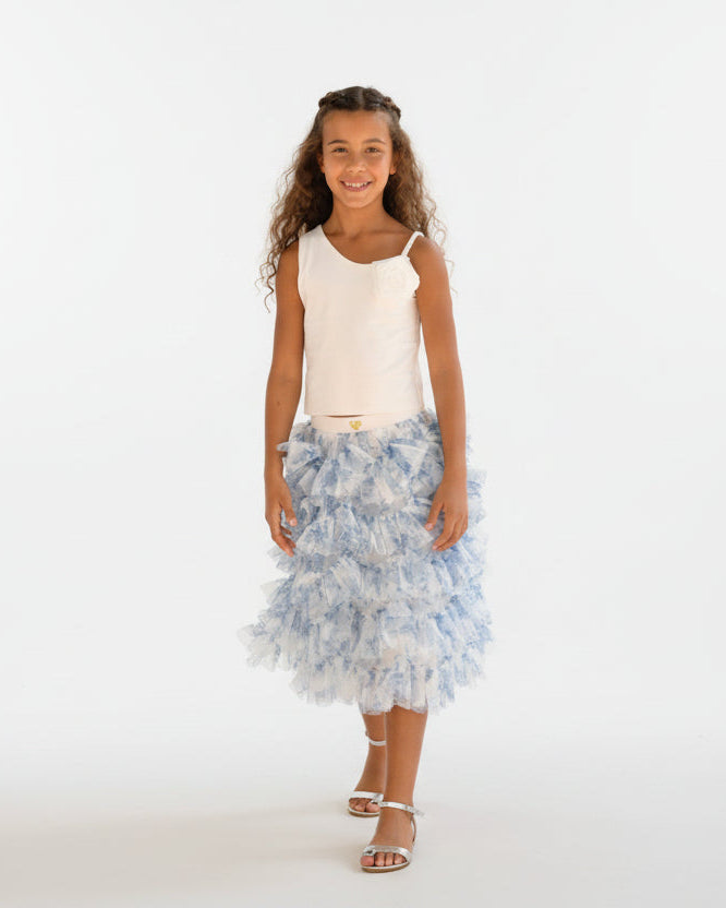 Young girl in a white top and blue floral skirt standing in front of a colorful wall.