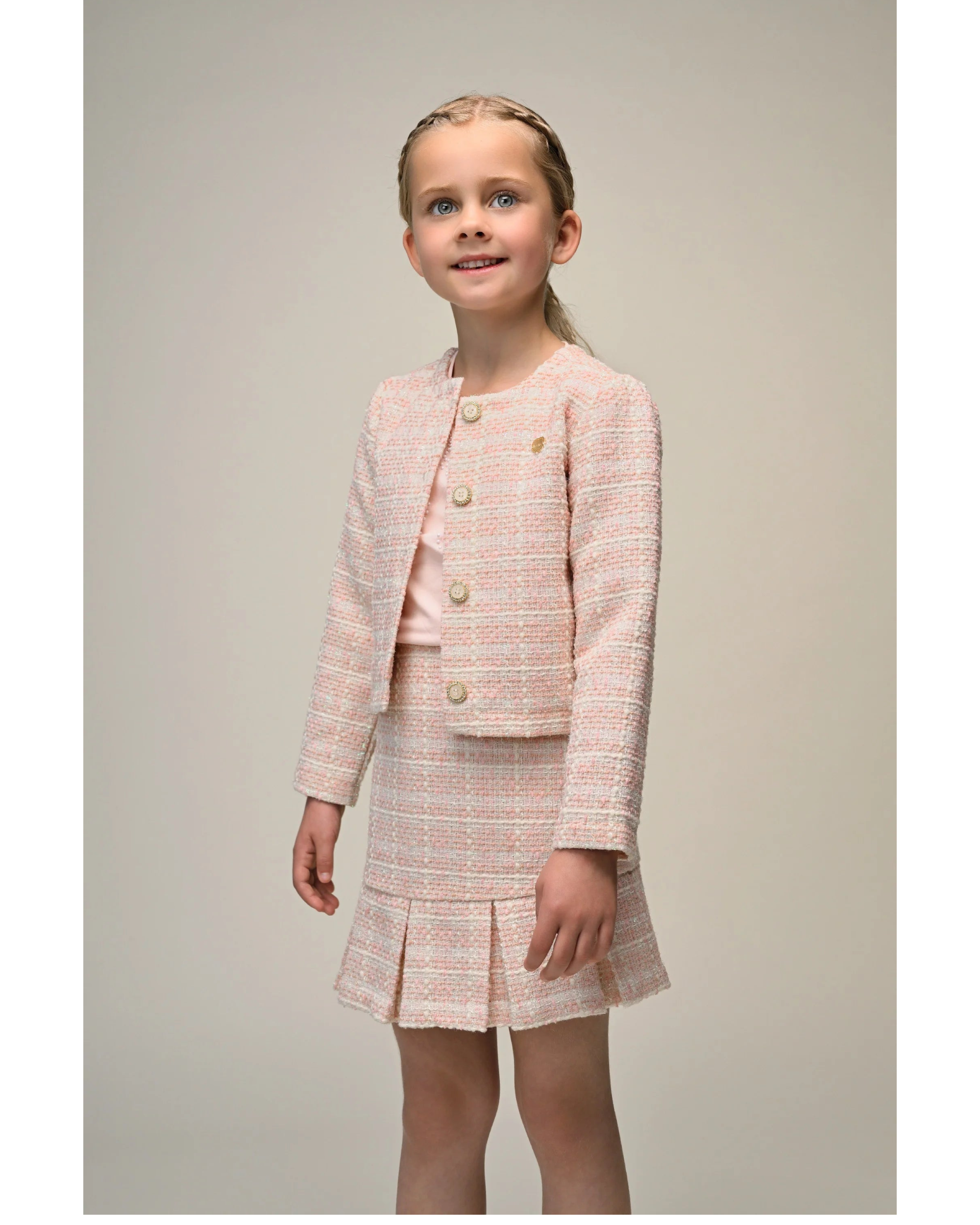 Young girl wearing a 
Le Chic pink tweed suit on a plain background