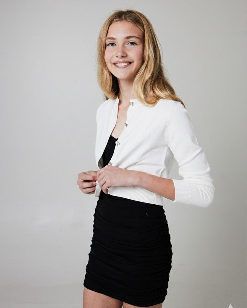 Tween  wearing a white cardigan with bow buttons over a black dress
