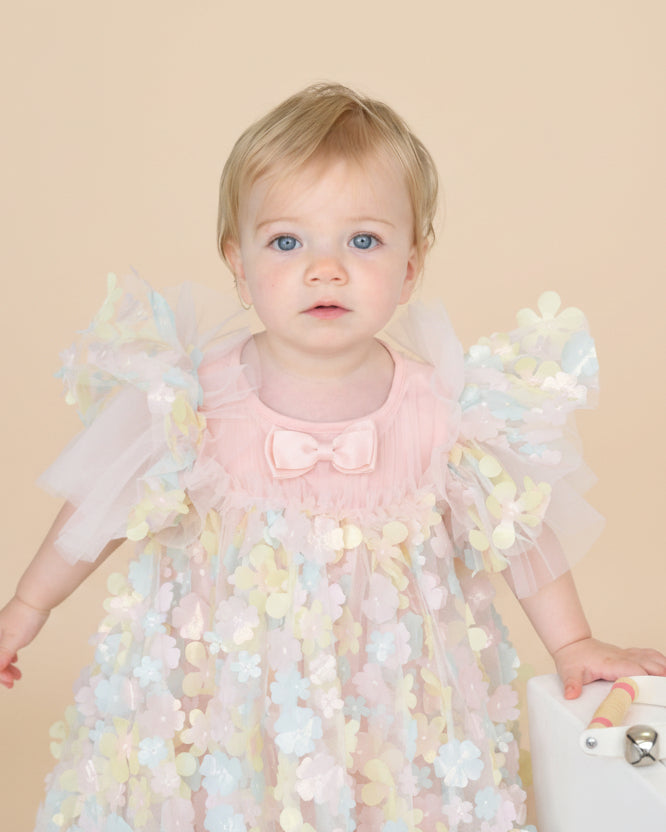 Baby in a floral dress with butterfly sleeves on a light background