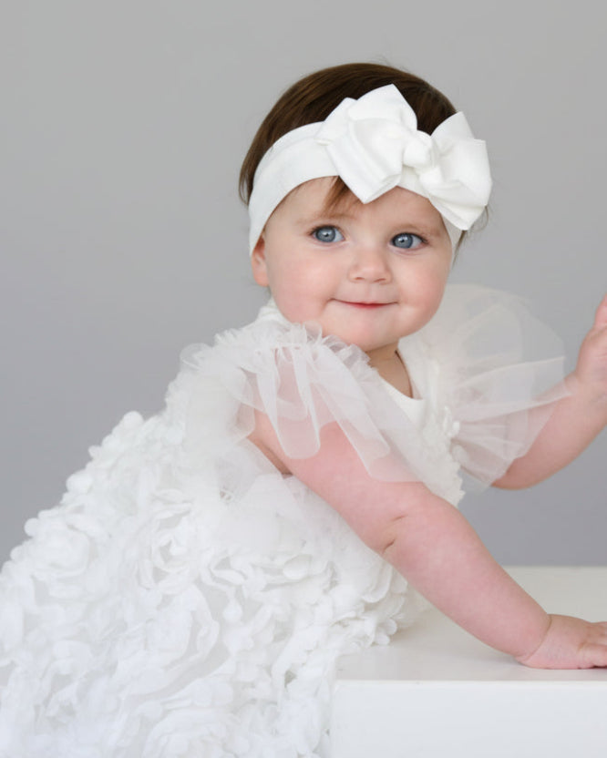 Baby in a white dress with ruffles and a matching headband on a white background