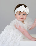 Baby in a white dress with ruffles and a matching headband on a white background