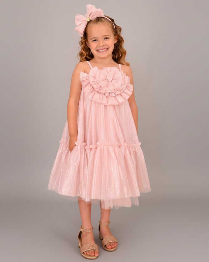 Young girl wearing a pink dress with ruffles standing on a wooden floor.