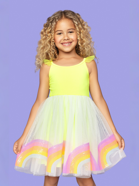 A young girl wearing a bright yellow dress with a rainbow of sequins on the skirt.